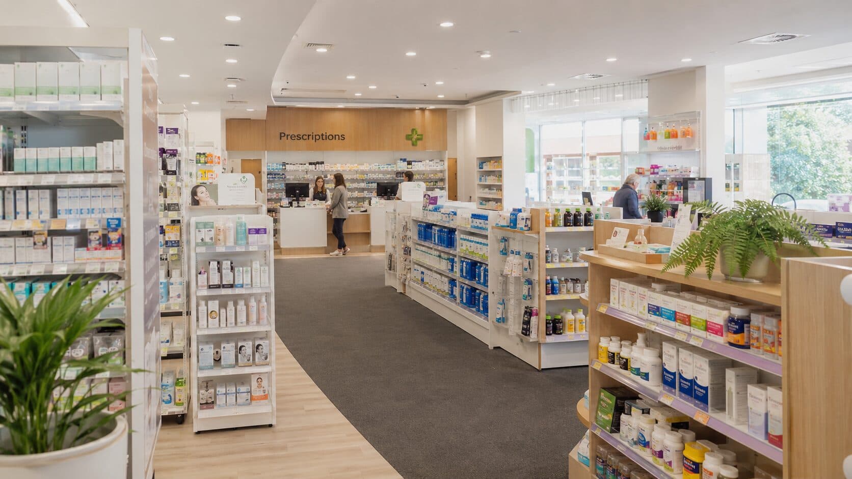 The bright, open interior of an Australian community pharmacy with a clearly signed prescriptions counter at the rear.
