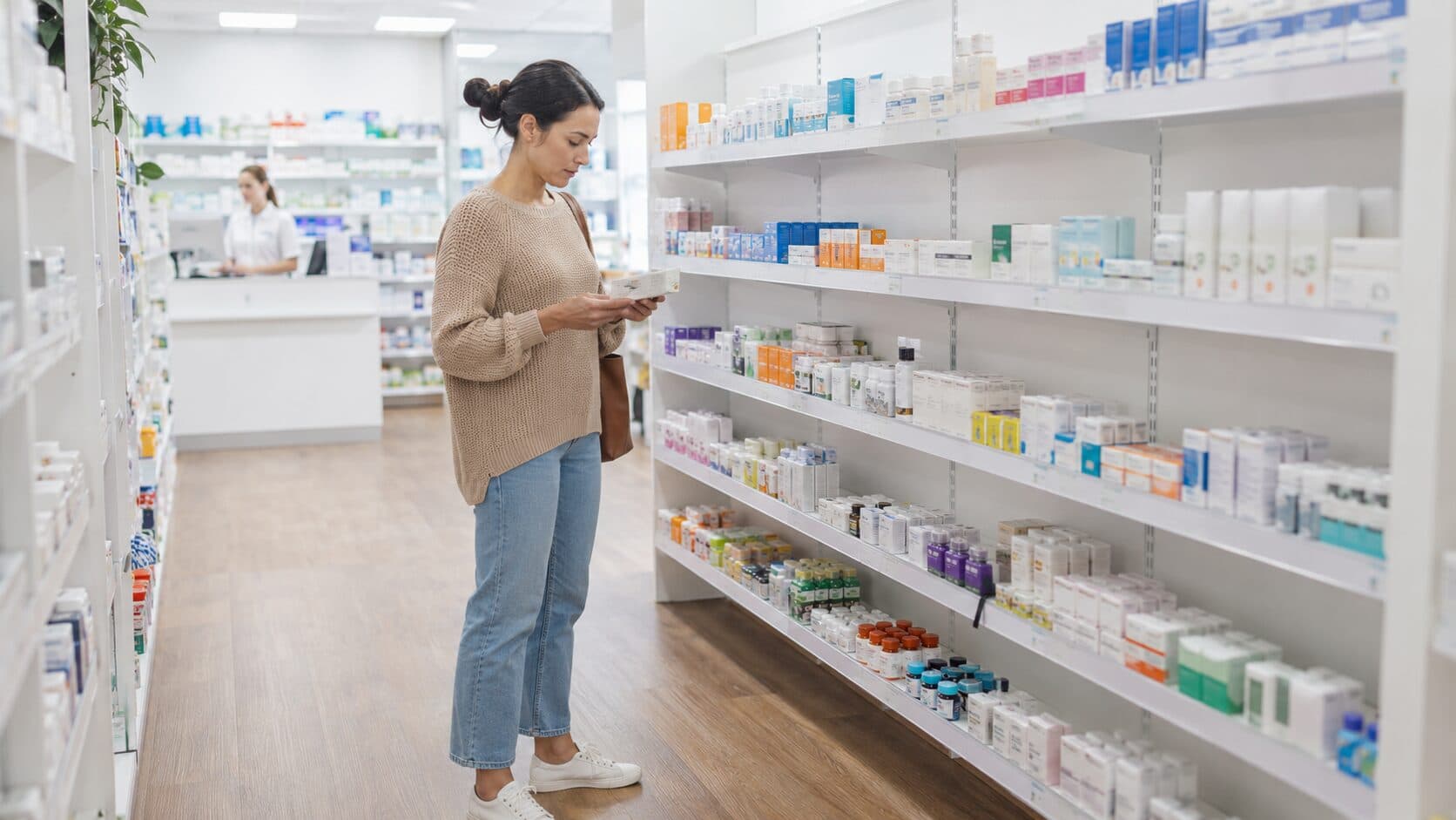 A customer reading a medicine box while browsing the brightly lit shelves of an Australian community pharmacy.