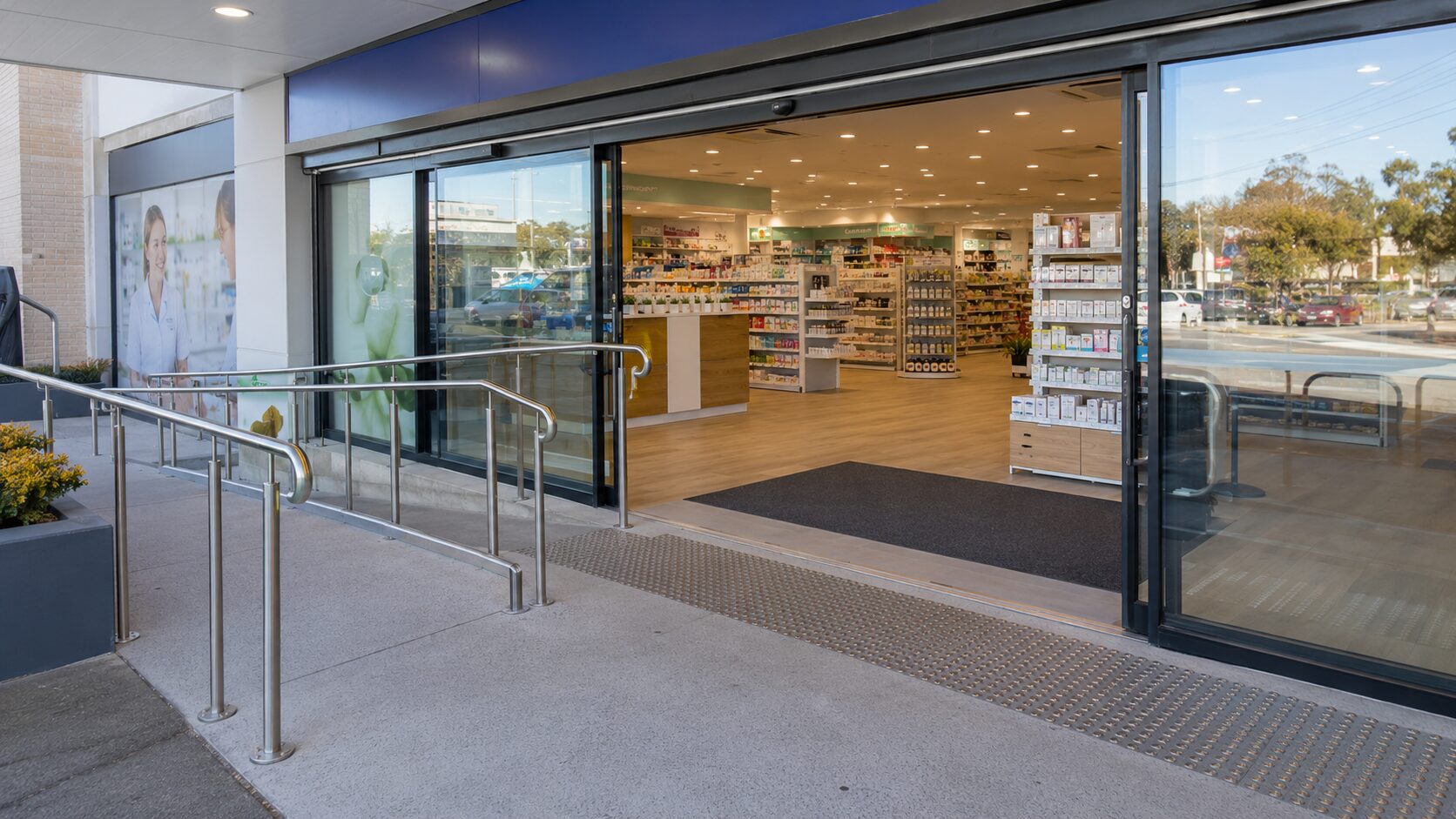 The step-free entrance of an Australian community pharmacy with a wheelchair-accessible ramp, handrails and automatic sliding doors.