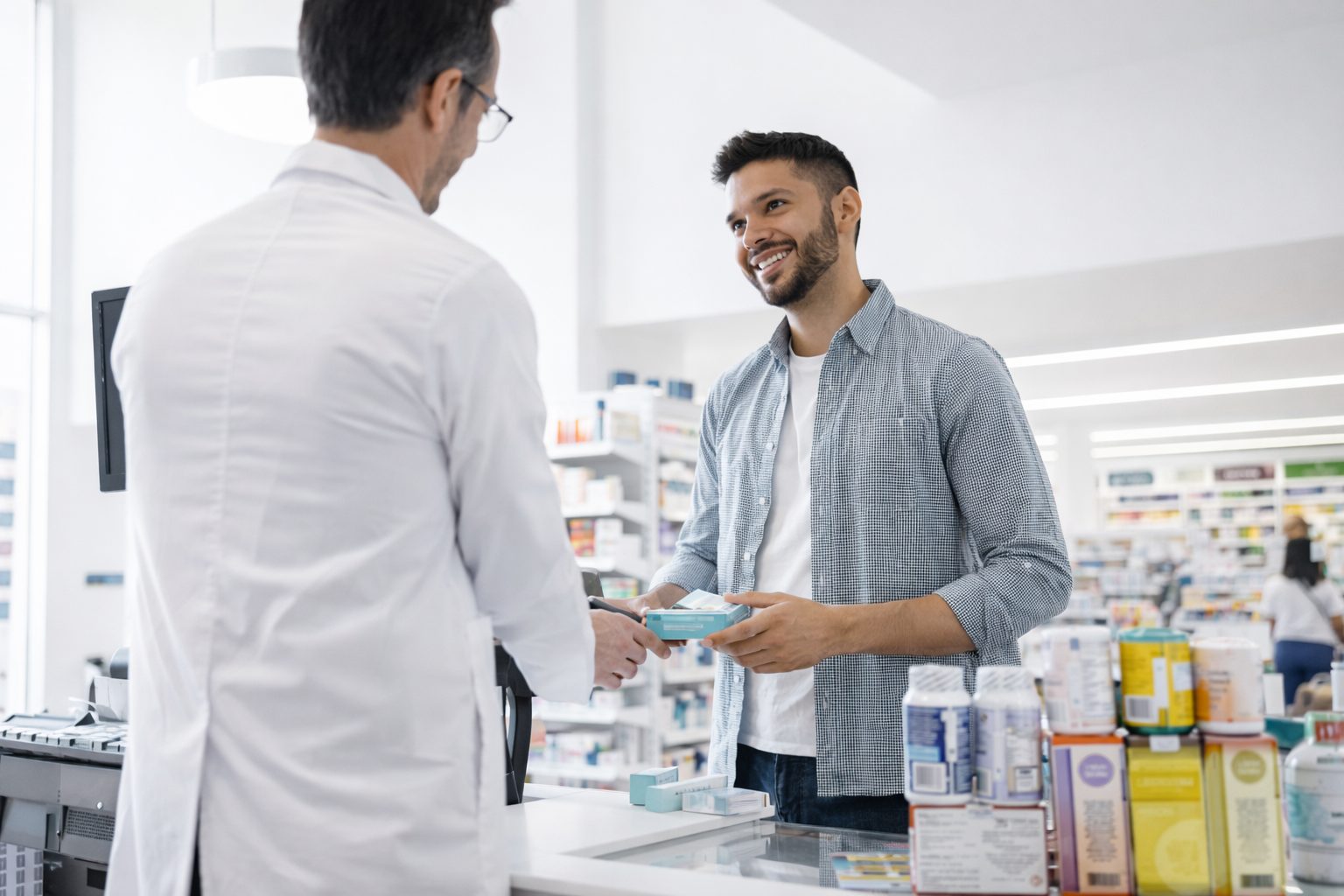 A customer being handed a paper pharmacy bag across the counter by a pharmacist in an Australian community pharmacy.
